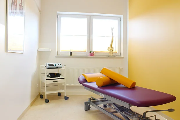Heller Behandlungsraum mit Therapieliege und Lagerungsrollen